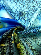 Folded Italian silk satin showing a blue patterned print, turquoise tones and touches of green.