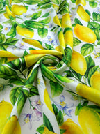 White silk satin fabric printed with yellow lemons, green foliage and delicate citrus flowers.