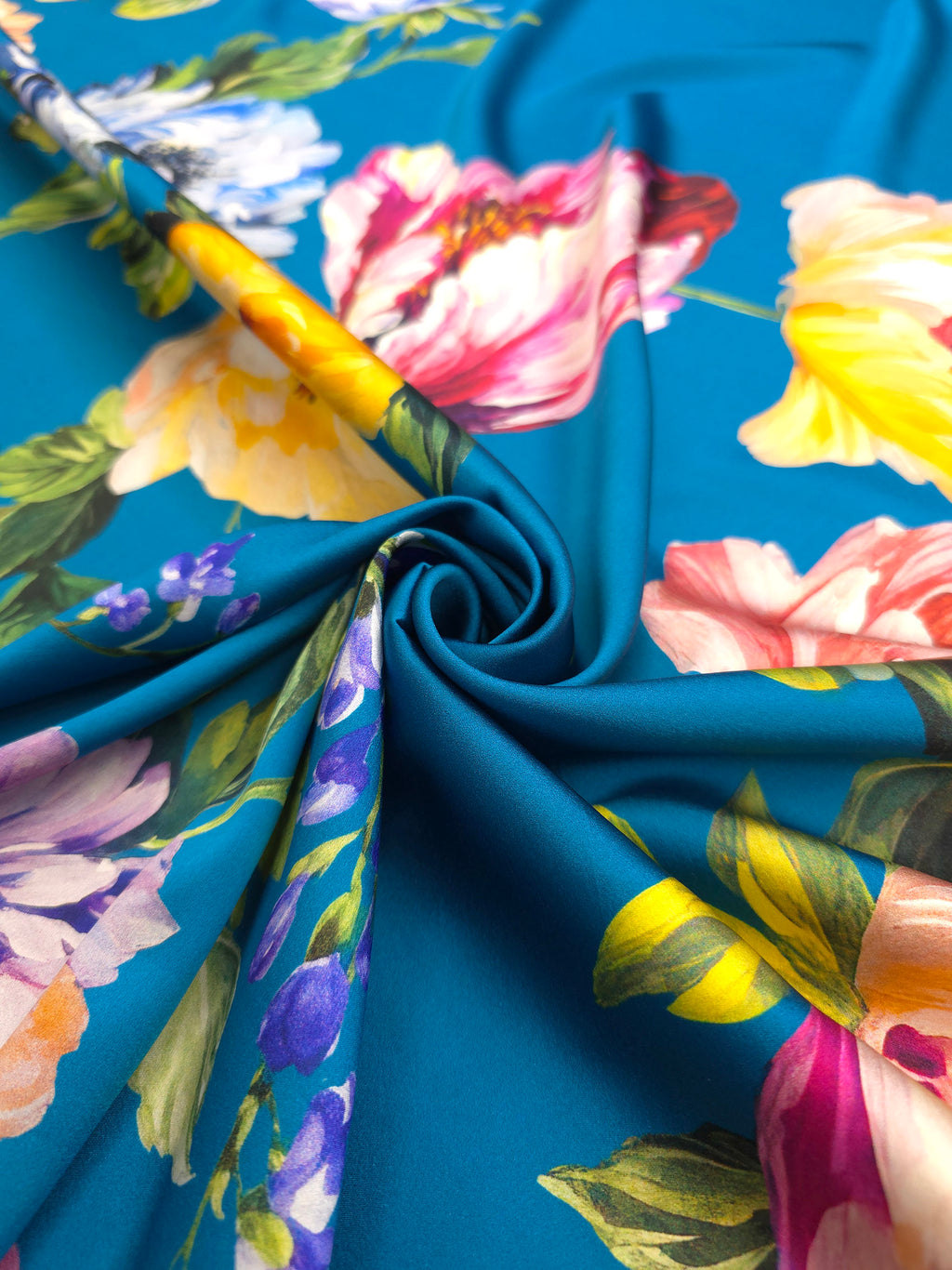 Italian printed silk satin with large yellow, pink and blue flowers arranged around a turquoise blue background.