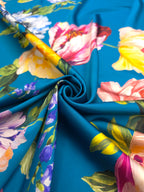 Italian printed silk satin with large yellow, pink and blue flowers arranged around a turquoise blue background.