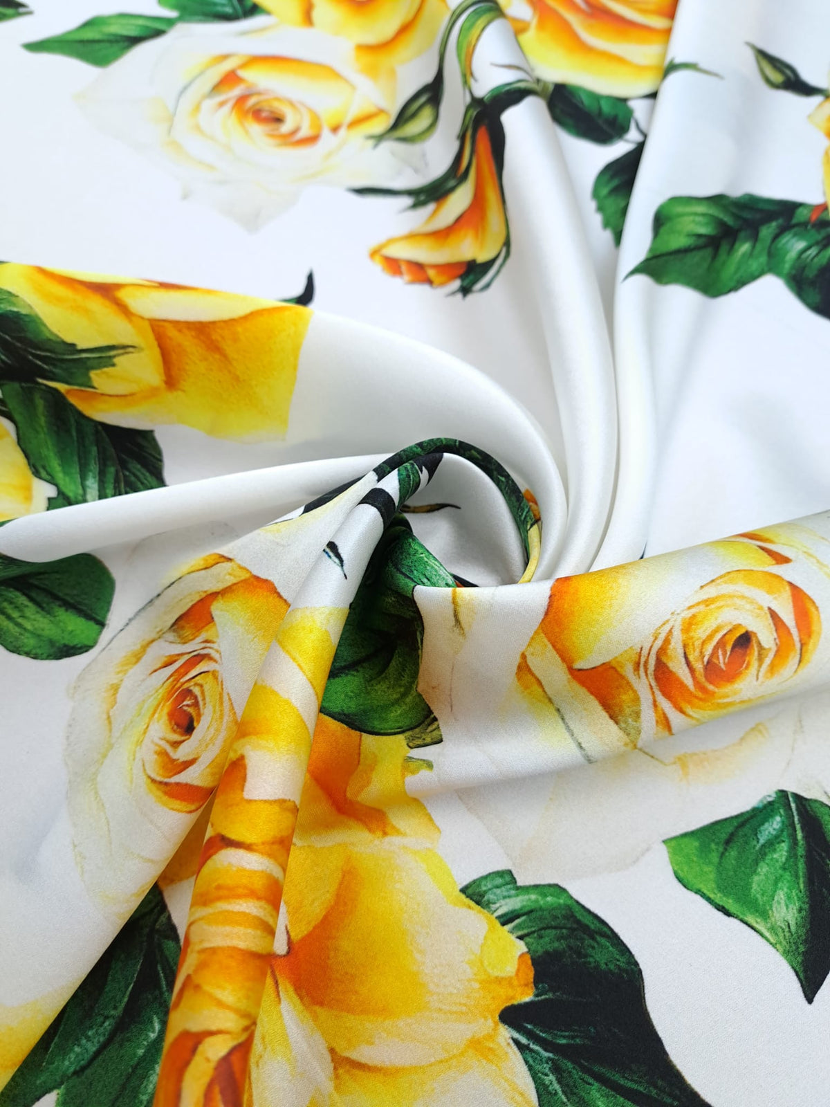 Lustrous silk satin printed with yellow and ivory roses and dark green leaves.